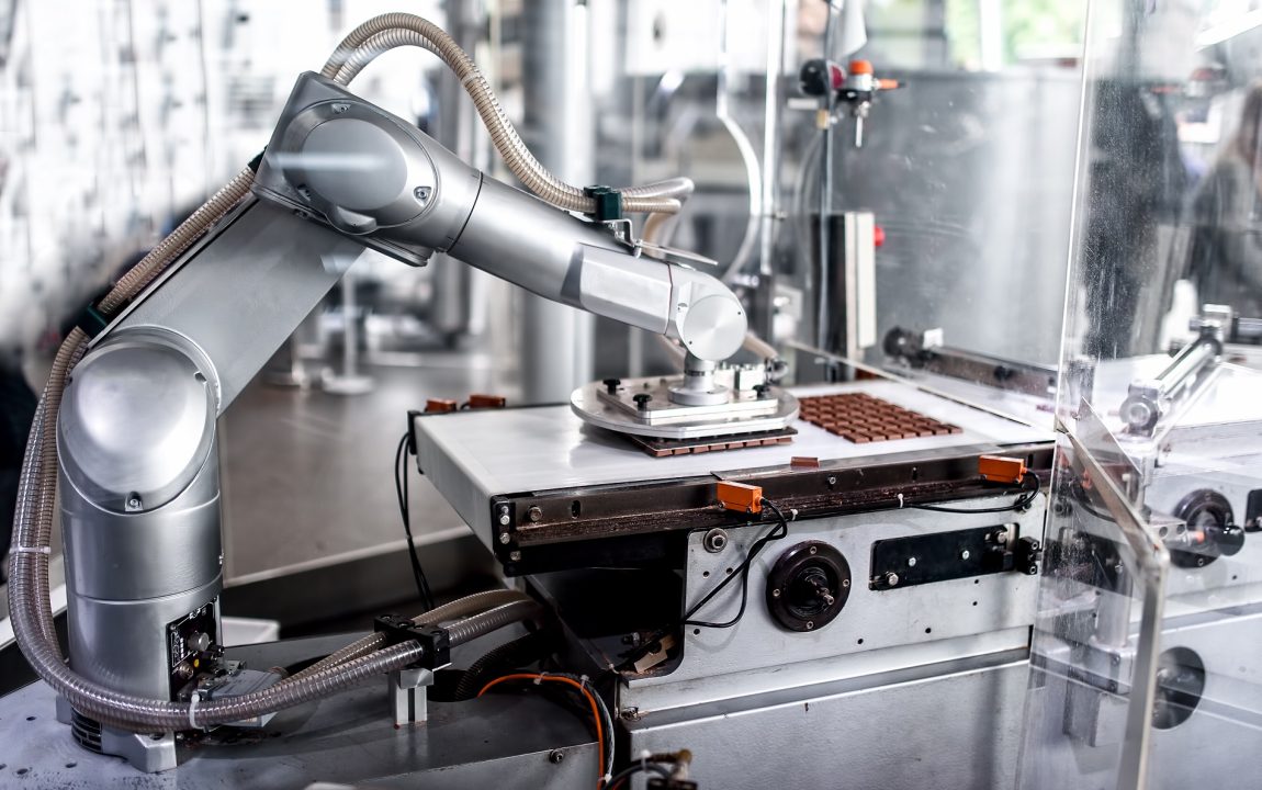 automatic robotic hand moving and preparing tiny bits of chocolate at chocolate factory. industrial chocolate factory with automatic robotic hand