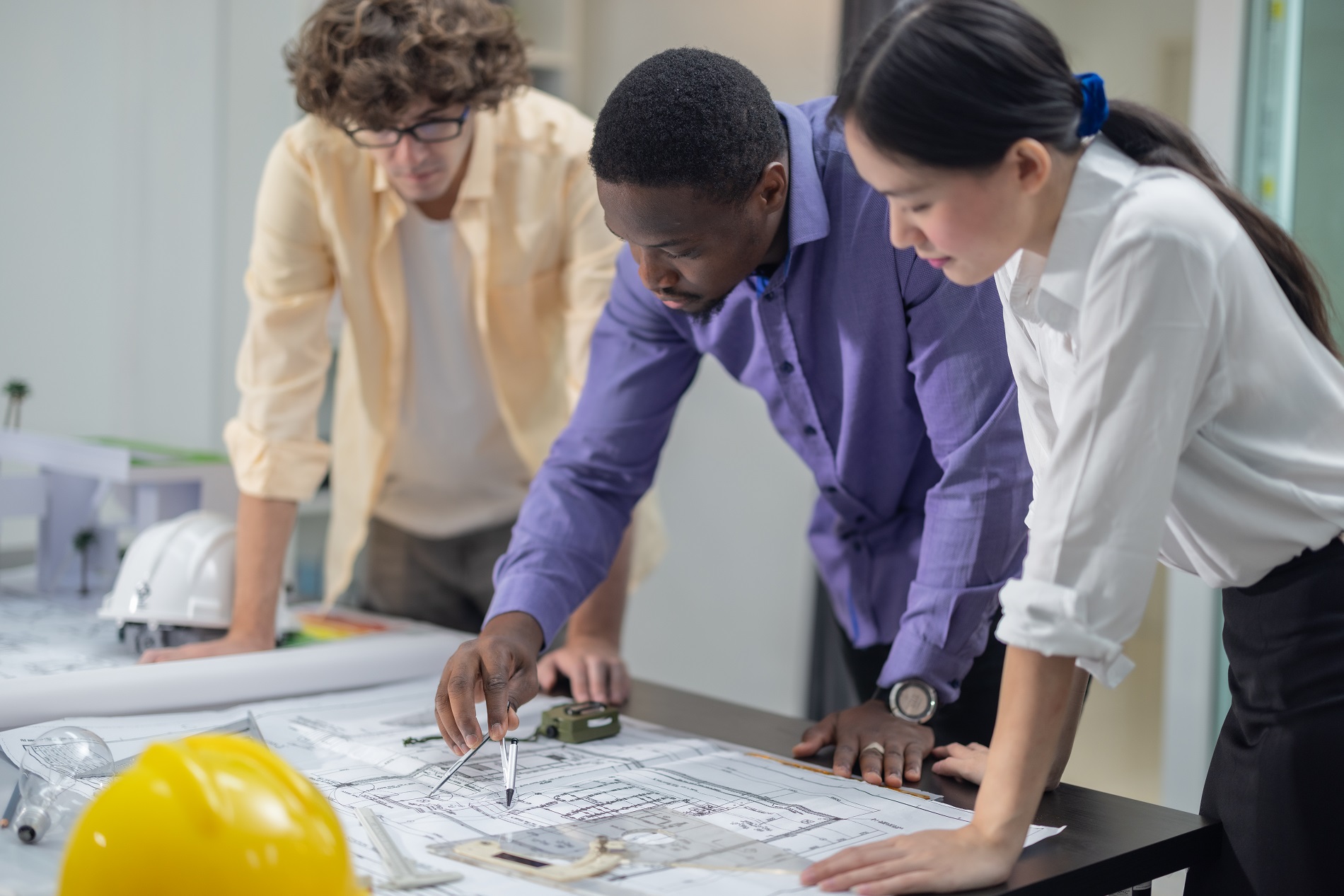 Multicultural team of architects collaborates on a low-carbon building project, analyzing blueprints, drafting layouts, calculating precise structures and materials for eco-friendly construction.